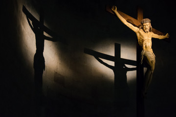 Antique wooden crucifix illuminated inside a historic Italian church with shadow cast on the wall