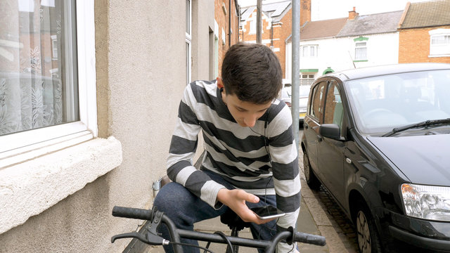 teen boy with smart phone listening or talking while sitting on bicycle british street. teenager and social media concept