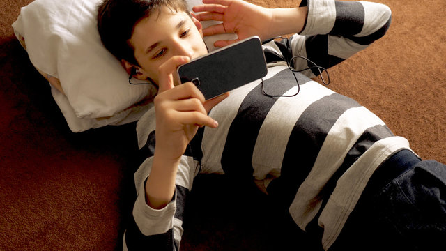 teen boy with smart phone listening or talking on sofa indoor. teenager and social media concept