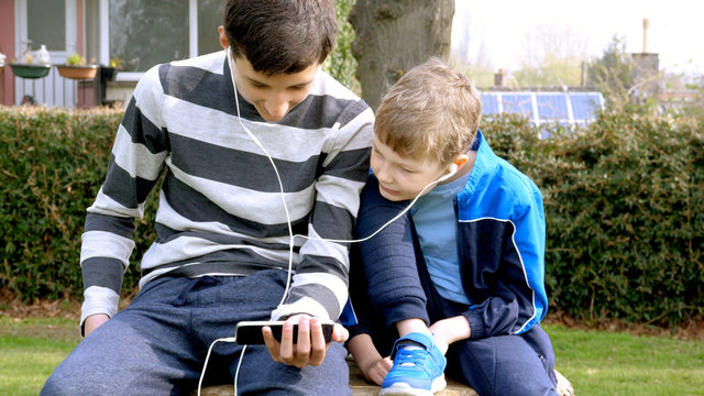 teen boys with smart phone listening or talking in british park on bench. teenager and social media concept
