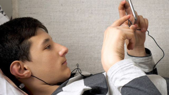 serious teen boy with smart phone listening or talking on sofa indoor. teenager and social media concept
