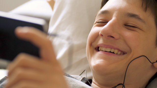 smiling teen boy with smart phone listening or talking on sofa indoor. teenager and social media concept