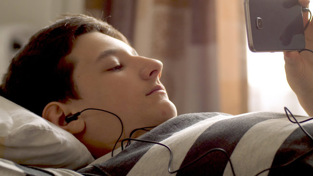 serious teen boy with smart phone listening or talking on sofa indoor. teenager and social media concept