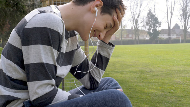 smiling teen boy with smart phone listening or talking while sitting in british park. teenager and social media concept