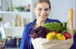 © lenets_tan - Young woman holding grocery shopping bag with vegetables .Standing in the kitchen