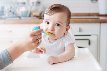 Wall Mural - Charming little baby boy 6-8 months eating first food pumpkin from spoon at home