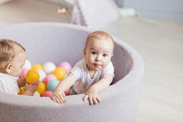 Cute little infants playing with colorful balls in soft playmat ball pit, dry pool. Little cute babies having fun in ball pit on birthday party at home.