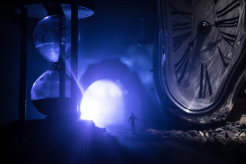 Time concept. Silhouette of a man standing between hourglasses with smoke and lights on a dark background. Surreal decorated picture