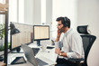 © Friends Stock - Always available. Side view of young bearded trader in headset talking with client and looking at monitor screen with trading charts and financial data while sitting in his modern office.