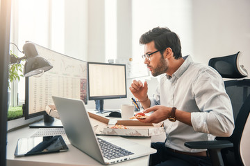 Fototapete - time for pizza! side view of young hungry trader is eating hot pizza while looking at monitor screen