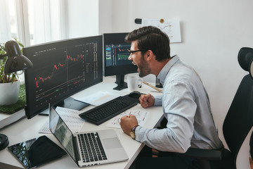 Poster - I am a winner! Happy young trader in formalwear and eyeglasses shouting and feeling excited while looking at trading charts and financial data in the office.