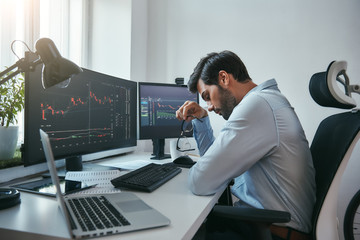 Fototapete - Time to take a break. Side view of tired young businessman or trader holding eyeglasses and feeling tired while working with data and charts on computers at his modern office.
