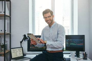 Fototapete - business success. cheerful young trader in formal wear is holding digital tablet and looking at came