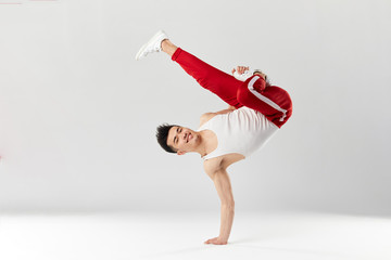 Athletic young b-boy standing on one hand while dancing break dance and doing downrock isolated over white studio background.