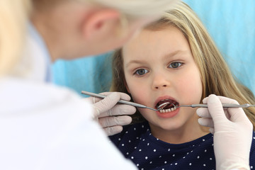 Little baby girl sitting at dental chair with open mouth and feeling fear during oral check up while doctor. Visiting dentist office. Medicine concept