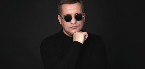  40 years man in trendy round sunglasses standing on black background