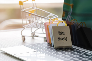 Colorful paper shopping bags leaning trolley on laptop keyboard. Consumer can buy products directly anywhere anytime from seller using web browser. Online shopping and e-commerce concept.