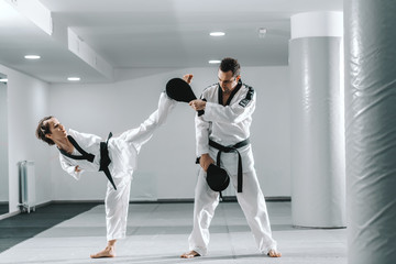 Wall Mural - Caucasian handicapped highly motivated girl practicing taekwondo with her training. Girl kicking kick target.