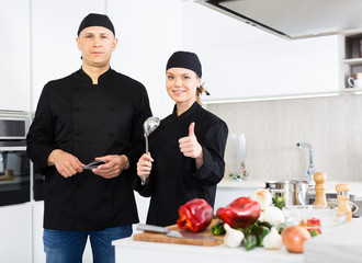 Wall Mural - Man and woman kitcheners in uniform are standing with devices in the kitchen