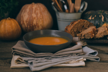 Wall Mural - Homemade autumn butternut squash soup with bread. Roasted pumpkin and carrot soup with cream and pumpkin seeds on white wooden background. Concept of healthy eating food. Copy space. Toned image.