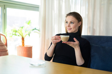 Wall Mural - beautiful young girl with make-up and hairstyle with a cup of coffee at a table in a restaurant