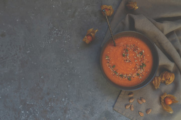 Seasonal autumn food. Spicy pumpkin ans carrot soup with cream and seasoning in rustic bowl on dark gray background. Hot, fresh vegetable soup. View from above with copy space. Toned image.