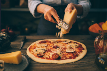 Food concept. Fresh original Italian raw pizza, preparation in traditional style. Making pizza. Female hands rubbed cheese grated on pizza, pizza cooking in a real home interior lifestyle and toning.