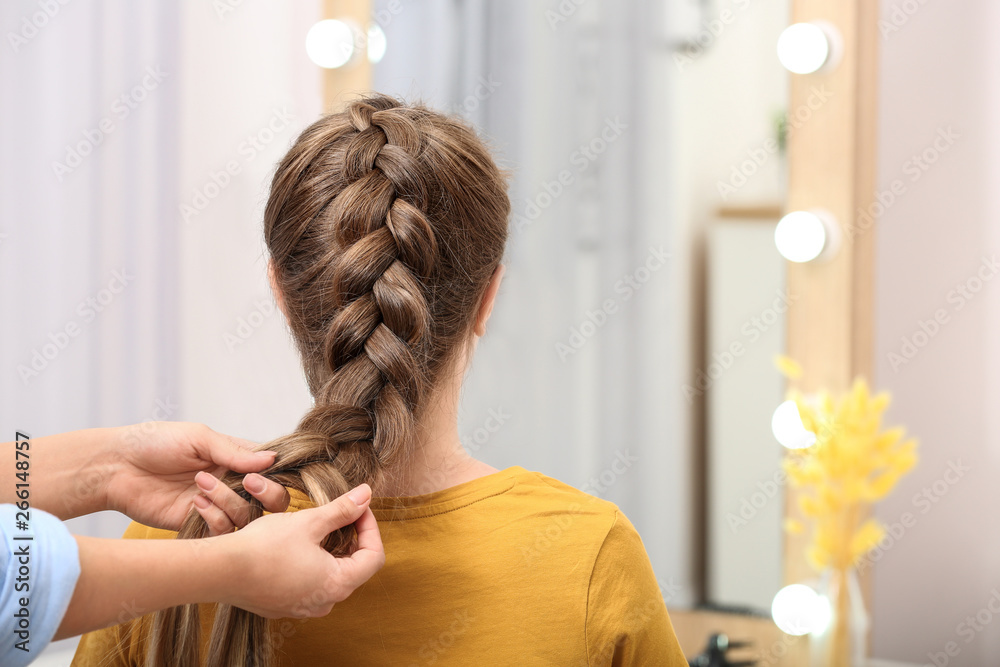 Professional coiffeuse braiding client's hair in salon - obrazy, fototapety, plakaty 