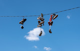 Fototapeta Sypialnia - Many pairs of sports shoes hung on a rope against a blue sky.
