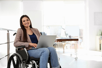 Portrait of young woman in wheelchair with laptop at office