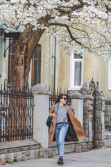 Wall Mural - young stylish woman walking by city street in coat blooming tree on background