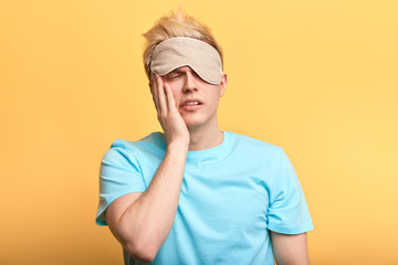 young sad unhappy man cannot wake up, get up in the morning. guy doesn't want to go to work. isolated yellow background