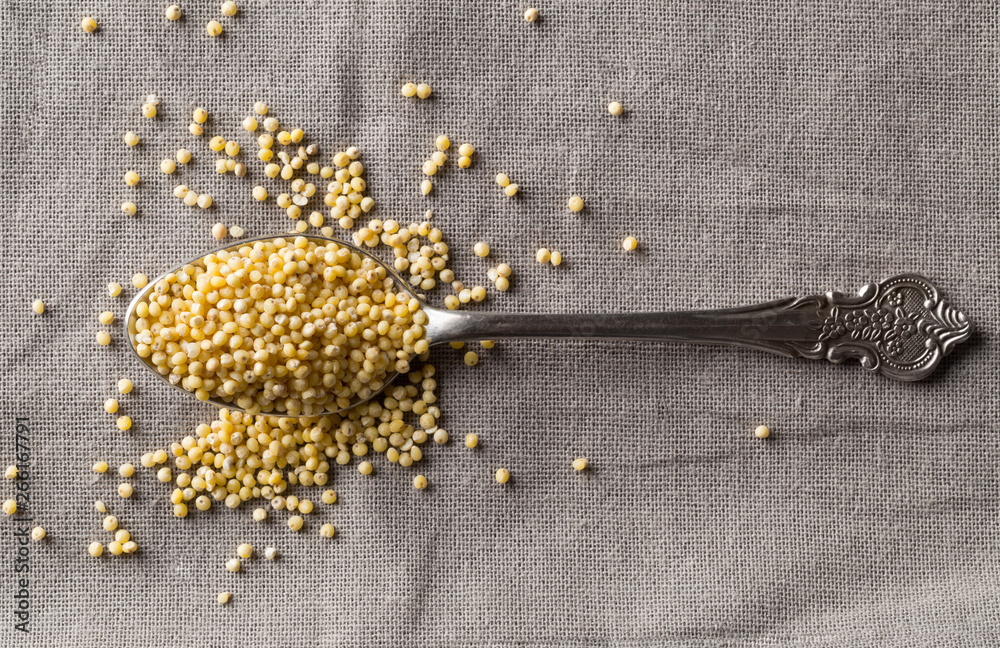 Pile of golden millet, a gluten free grain seed, in metal spoon on grey fabric background - obrazy, fototapety, plakaty 