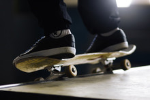 A Man In Black Pants And Black Sports Shoes On A Skateboard Does A Slip-on Trick On A Ramp In The Park
