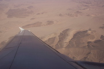 wing of airplane in sky with clouds and sun