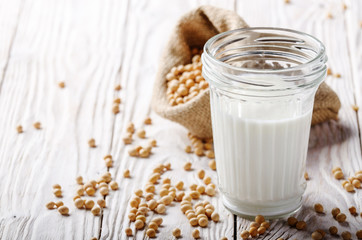 Poster - Non-dairy alternative Soy milk or yogurt in mason jar on white wooden table with soybeans in hemp sack