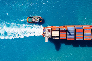 Wall Mural - Tugboat parks in port Cargo ship with containers against blue sea, top view. Logistics delivery concept