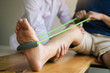 © wutzkoh - Patient use resistance band stretching out his leg with physical therapist helps in clinic room.