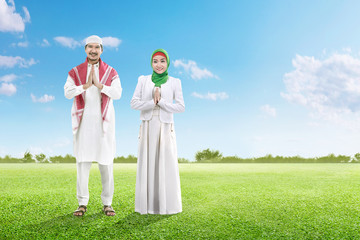 Wall Mural - Asian muslim man with cap and muslim woman with veil praying together on the green grass field