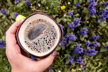 Cups of coffee in female hand in flower. Outdoors. Place for text.