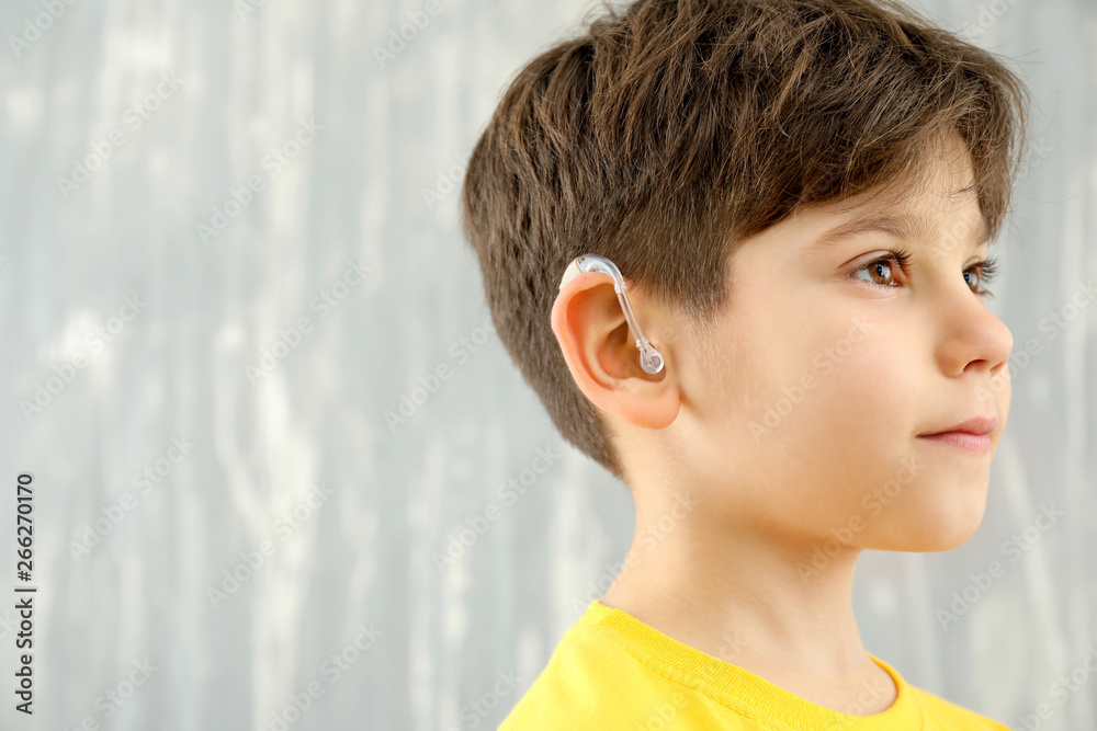 Little boy with hearing aid on grey background
