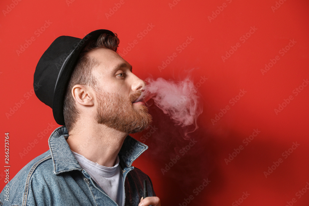 Young man smoking on color background