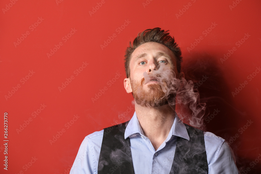 Young man smoking on color background