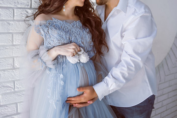 pregnant girl in a blue dress with her husband hugging and holding her belly