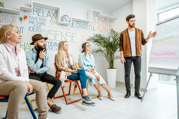 Wall Mural - Group of diverse people during the psychological seminar with male coach showing on flipchart in the office