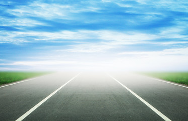 Background of blurred asphalt road, clear blue sky with clouds. Sunlit skyline