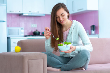 Wall Mural - Young happy vegan woman eating vegetable salad for lunch at home. Diet and fitness eating. Clean and healthy food