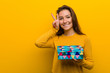 © Asier - Young european woman holding a gift showing victory sign and smiling broadly.