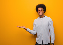 Young African American Man Over An Orange Wall Holding Something With Hand