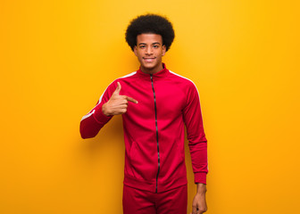 Wall Mural - Young sport black man over an orange wall person pointing by hand to a shirt copy space, proud and confident